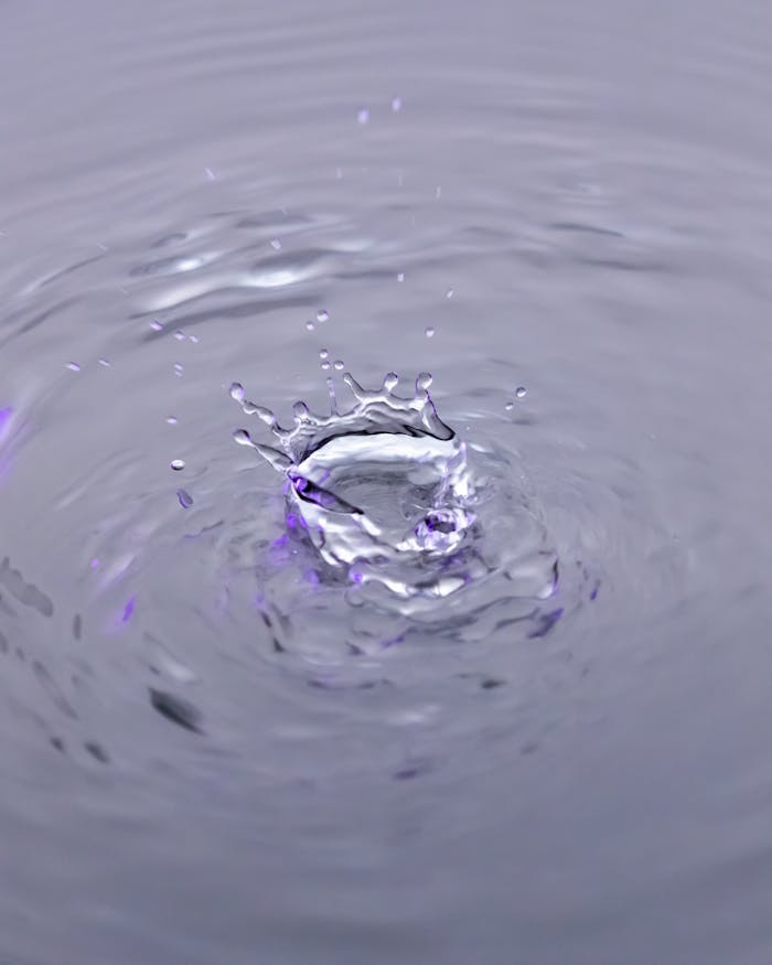 Close-up of a water droplet splash with violet hues radiating ripples.